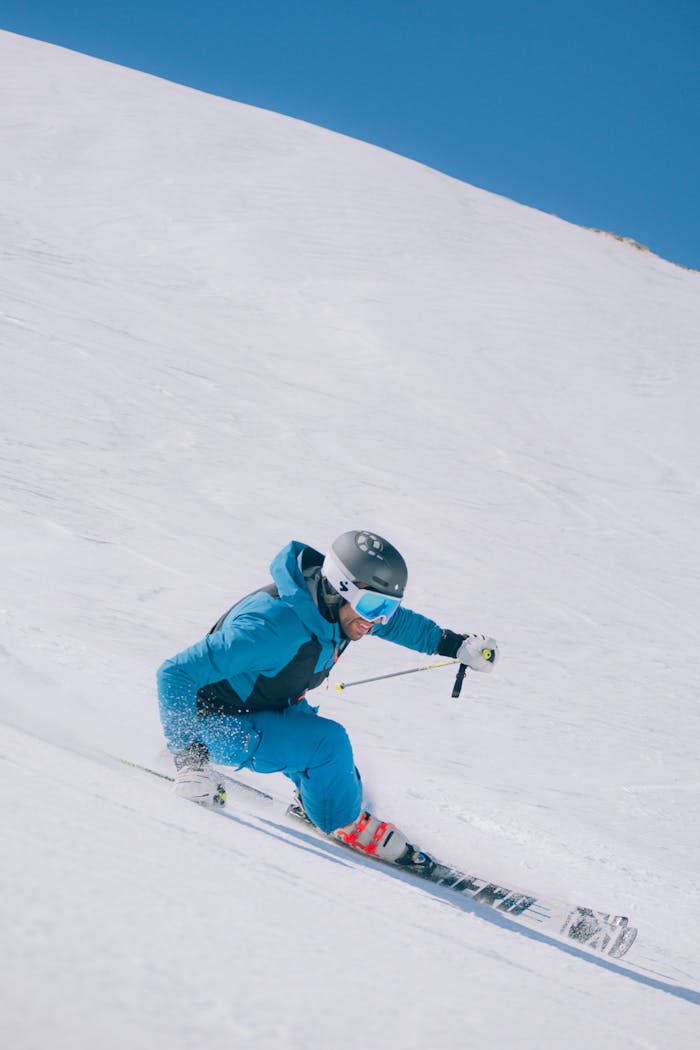 Skier in blue gear carving down snowy slope in Abruzzo, Italia during winter.