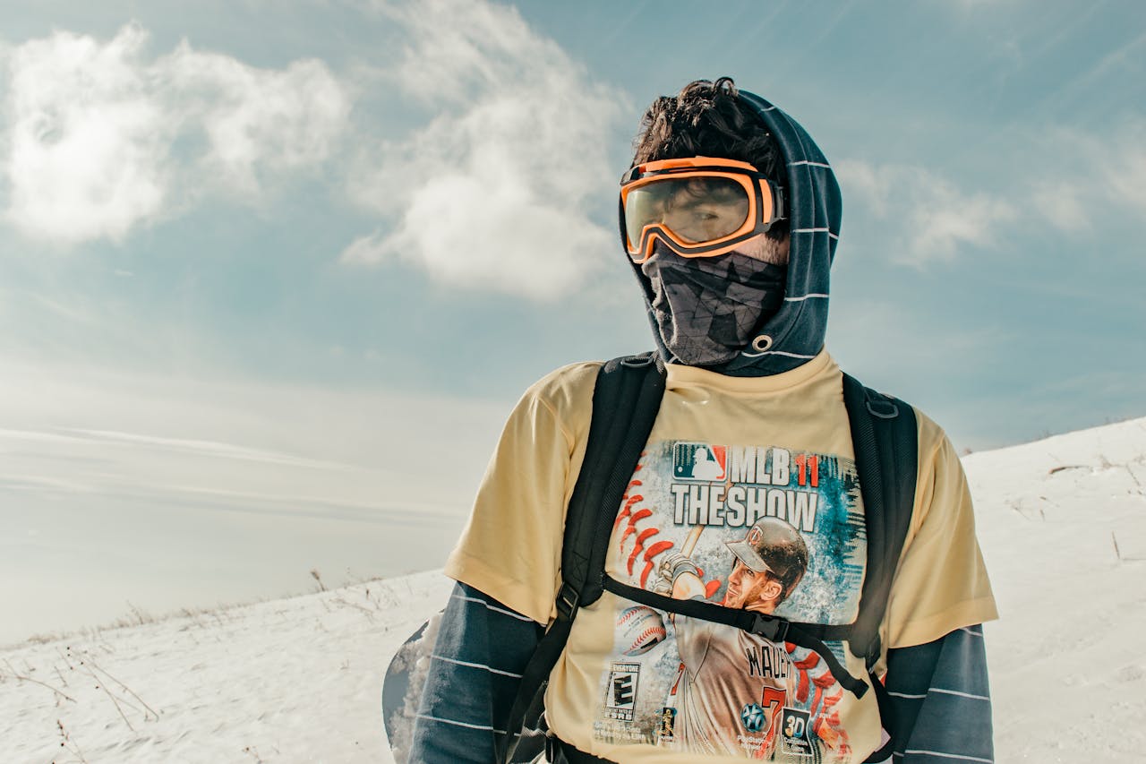 A person in winter attire with goggles standing in a snowy landscape, ready for adventure.