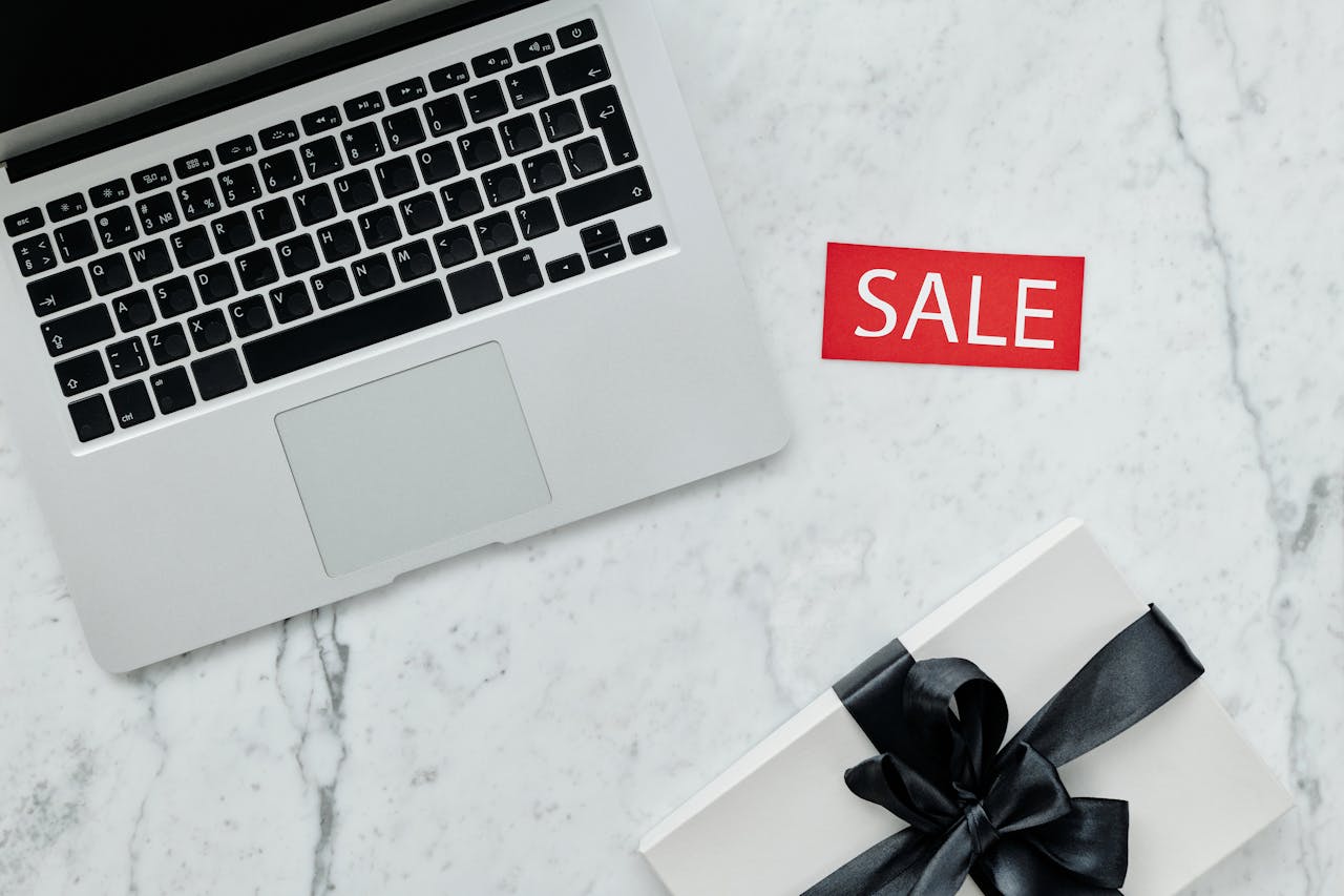 Top-down view of a laptop and gift with a sale sign on marble background.